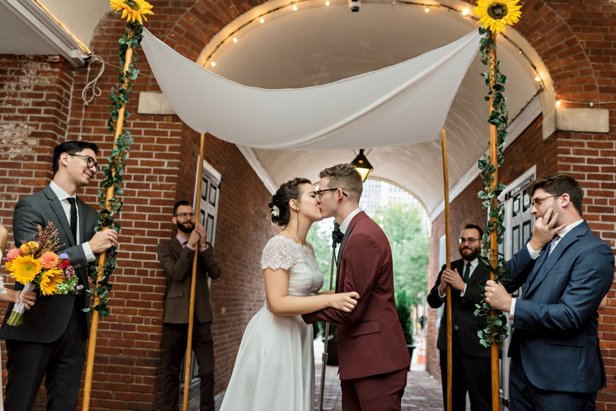 A bride and groom kiss under a chuppah at the end of their wedding ceremony.